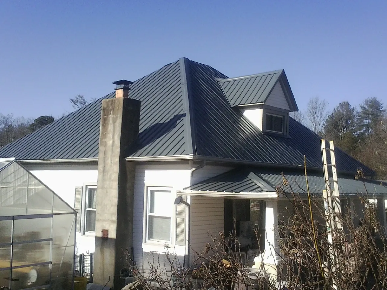 Dark blue standing seam metal roof on a white farmhouse with dormer — Slate & Tile Roof Repair by Roofing Brothers in Kingsbury
