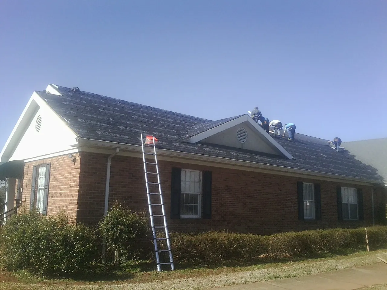 Crew tearing shingles off a brick ranch roof with a ladder set — Emergency Roof Repair work by our crew in Kingsbury