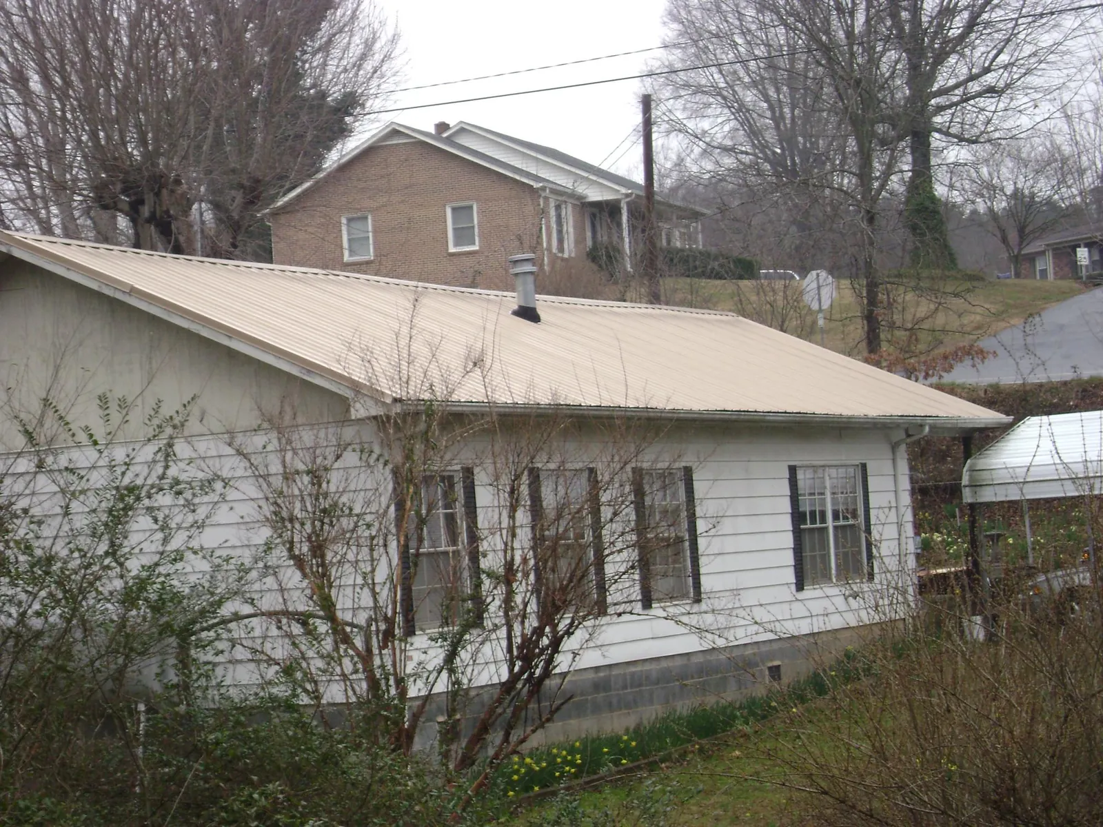 Tan metal roof on a white sided house set into a hillside — Commercial Roofing by Roofing Brothers in Kingsbury